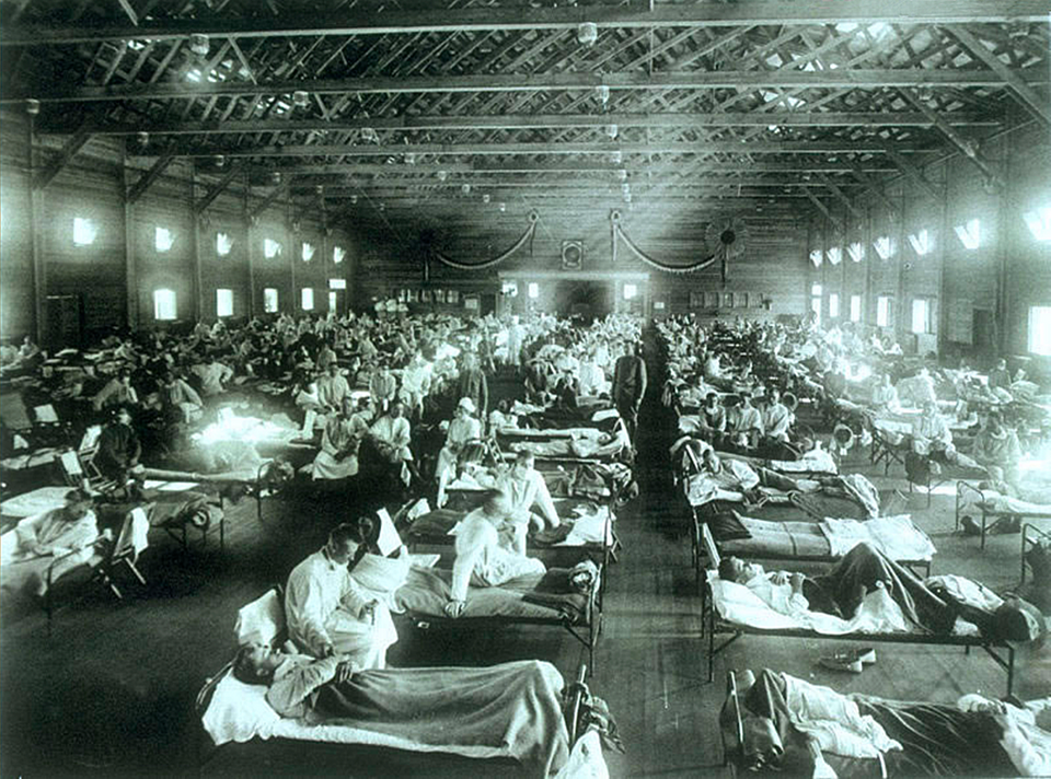 Black-and-white view of a crowded military hospital ward with rows of beds and patients during the 1918 influenza pandemic.